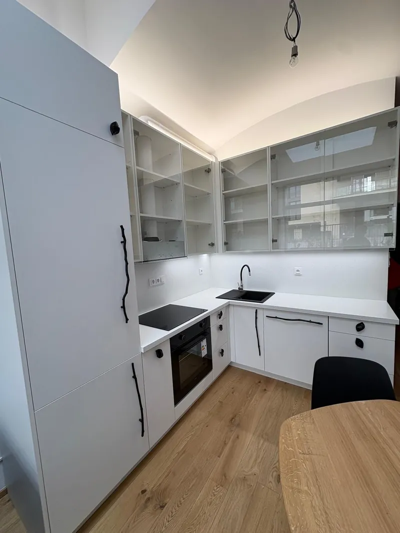 Kuchyň do L pod klenutým stropem s prosklenými horními skříňkami a bílou pracovní deskou