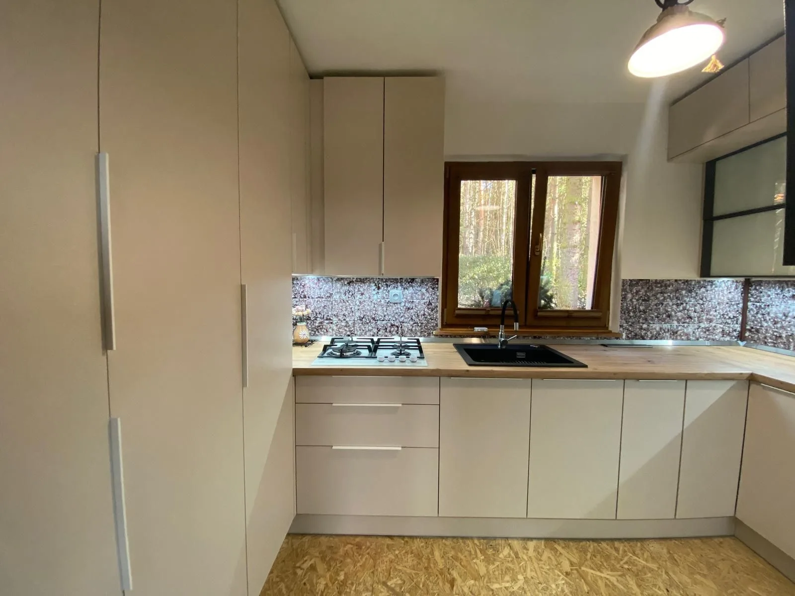 Vysoká béžová skříň a kuchyňská linka na chatě s osvětlením pod horními skříňkami
